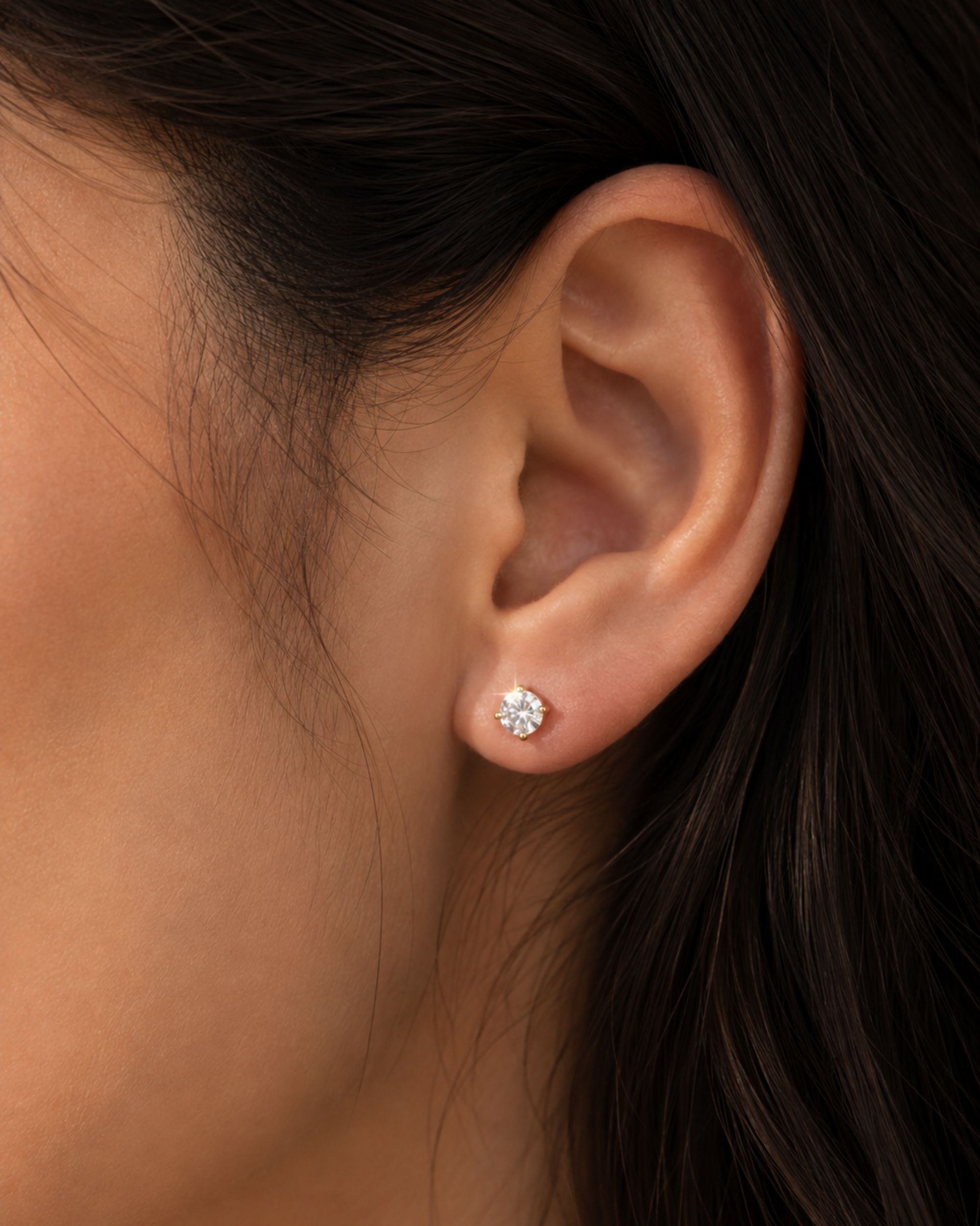 A close-up of a person's ear wearing a small round stud earring with a clear gemstone in a silver-toned setting.