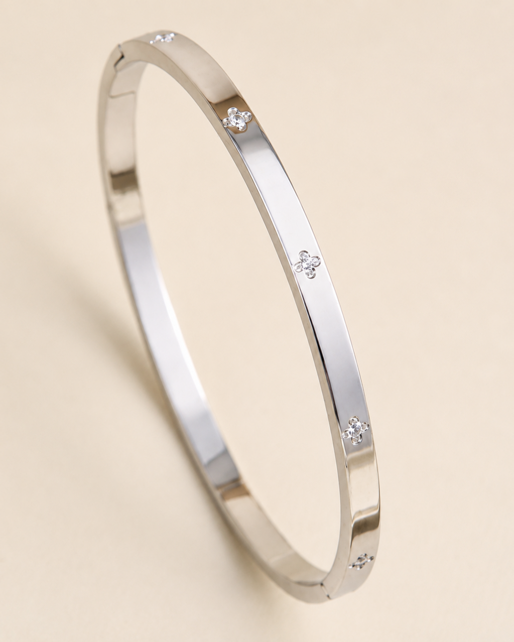 A polished silver-toned bangle bracelet with small diamond-like accents spaced along the outer band, photographed on a warm light beige background.