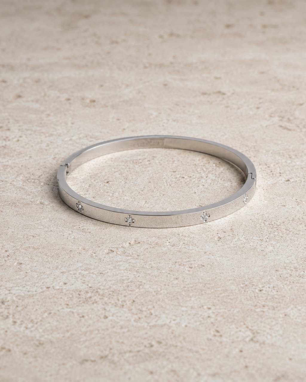 A thin silver bangle bracelet with small star motifs set along the band, resting on a textured beige stone surface.