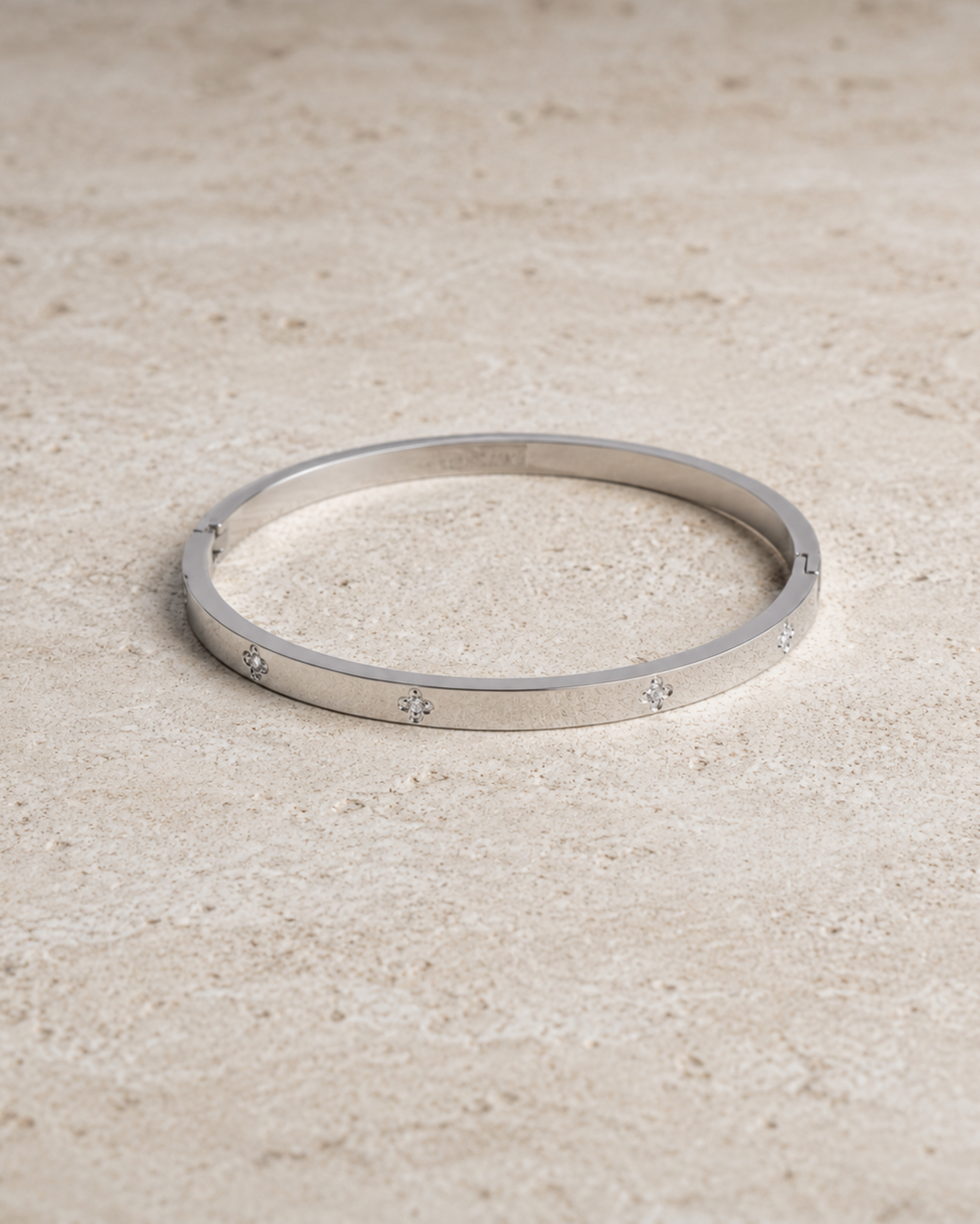 A thin silver bangle bracelet with small star motifs set along the band, resting on a textured beige stone surface.