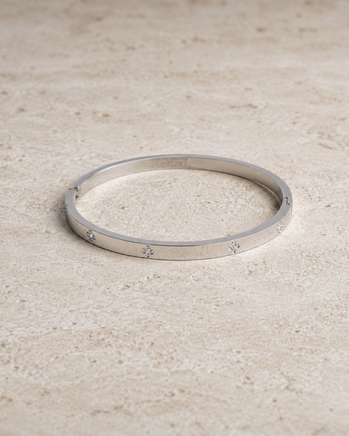 A thin silver bangle bracelet with small star motifs set along the band, resting on a textured beige stone surface.