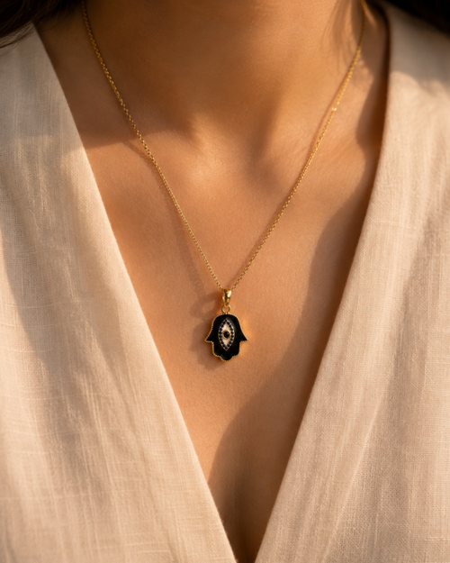 Gold necklace with a black pendant worn by a person in a white blouse.