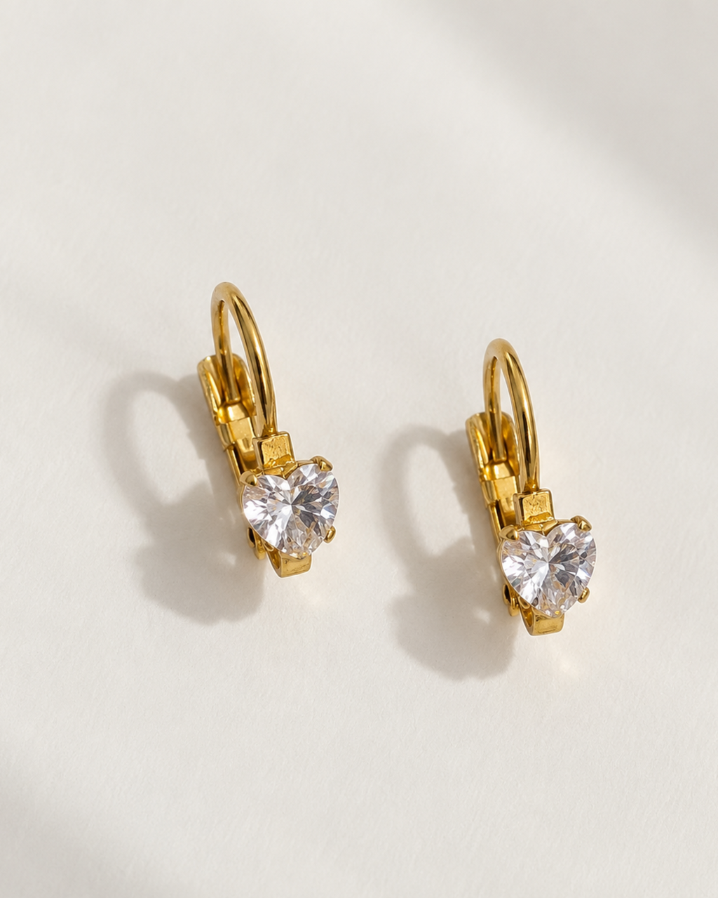 A pair of gold leverback earrings with heart-shaped clear gemstones, displayed on a clean white surface with soft shadows.