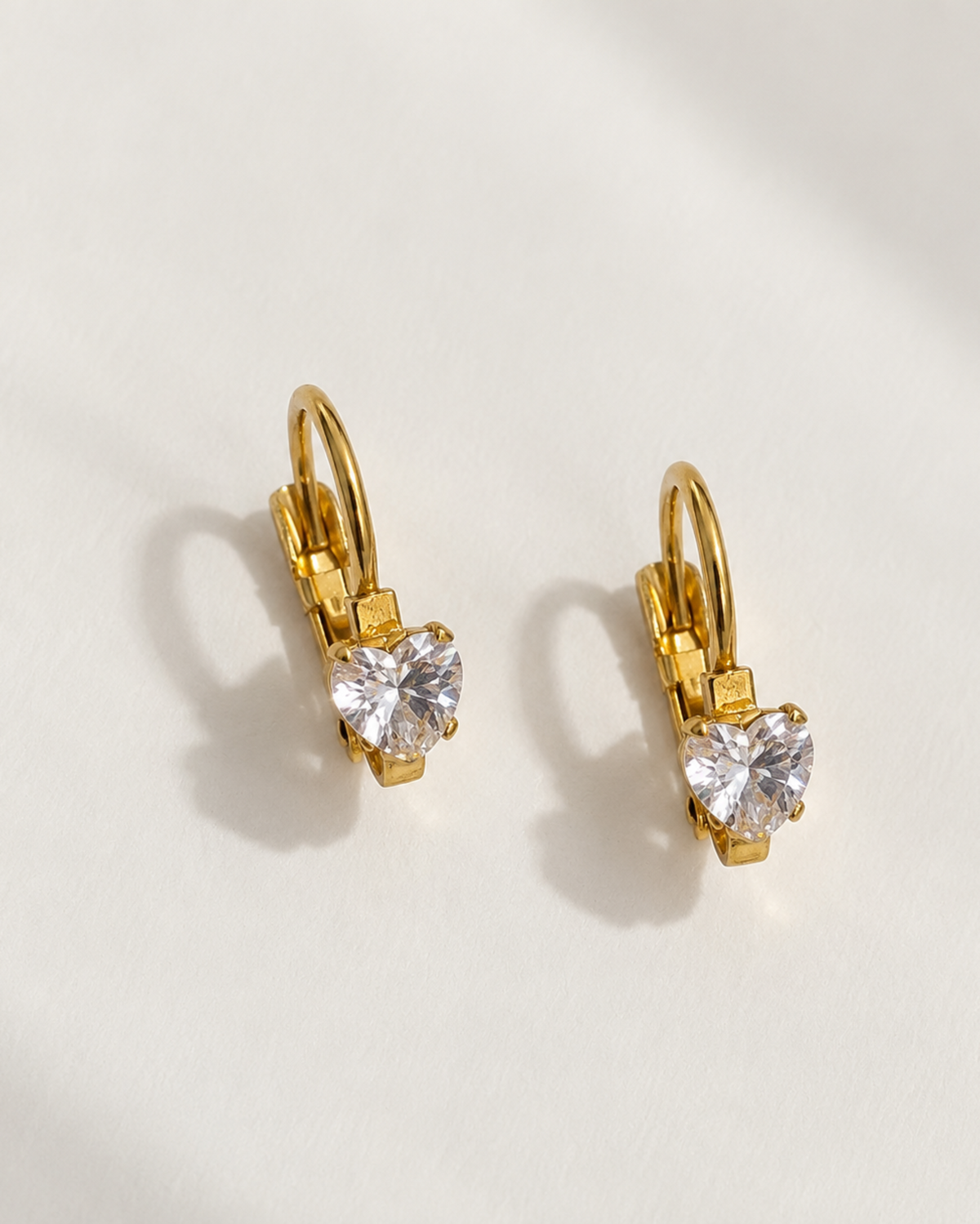 A pair of gold leverback earrings with heart-shaped clear gemstones, displayed on a clean white surface with soft shadows.