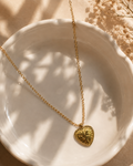 Gold necklace with a heart-shaped pendant on a white dish with a beige background