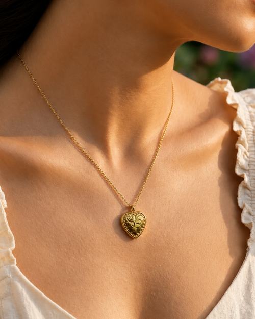 Woman wearing a gold necklace with a heart-shaped pendant, outdoors.