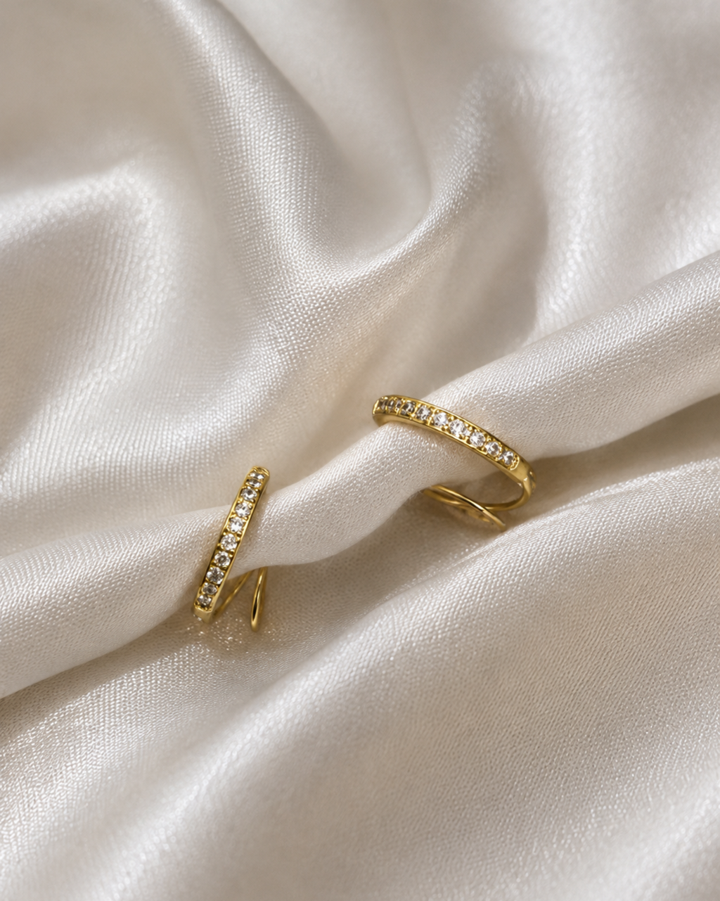 Two gold rings set with small clear stones, displayed on draped white satin fabric.