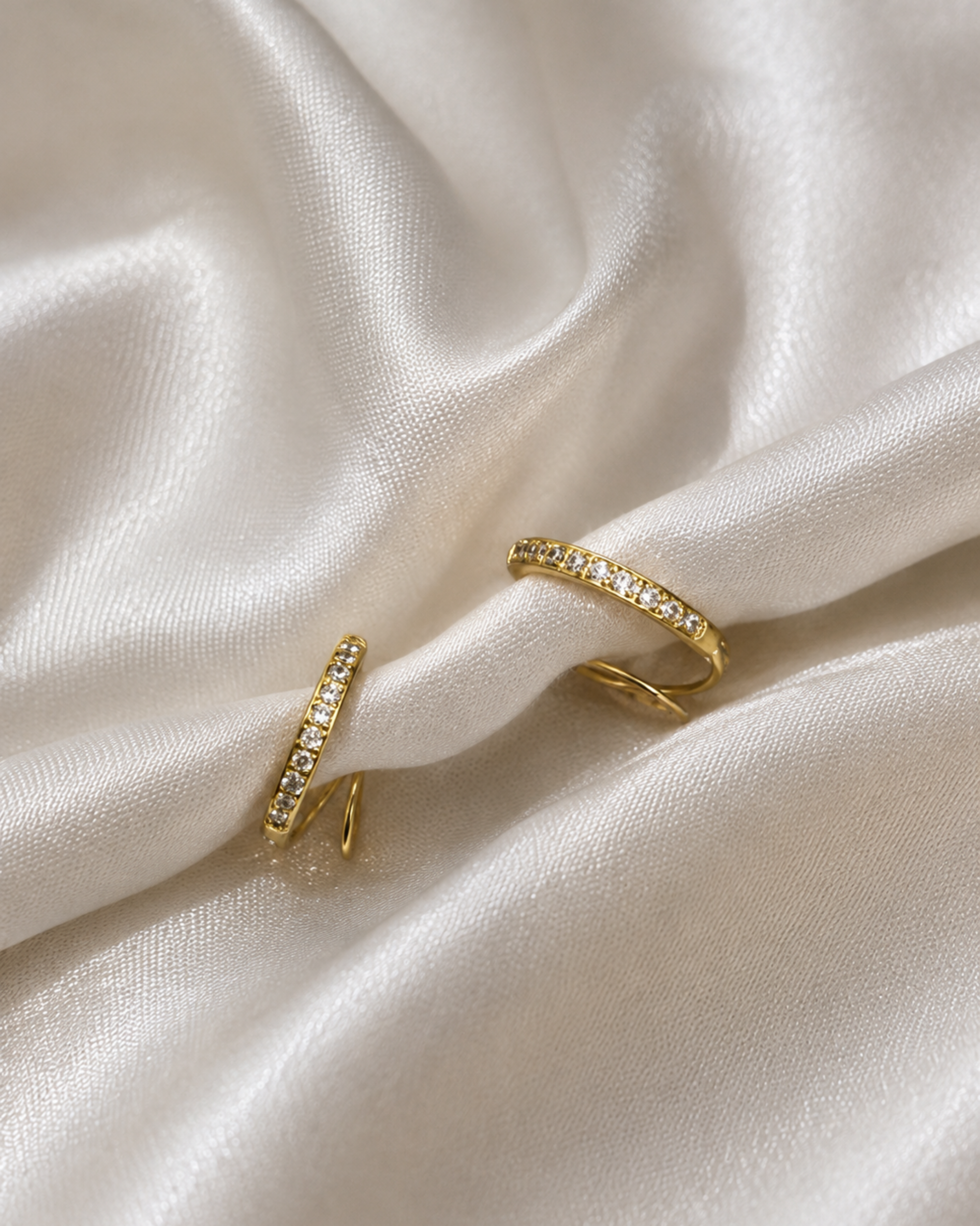 Two gold rings set with small clear stones, displayed on draped white satin fabric.