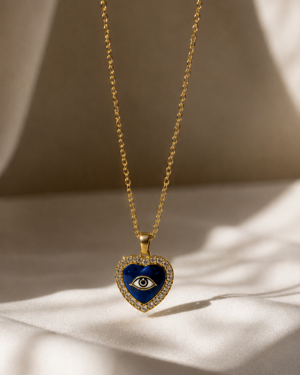 Gold necklace with a blue heart-shaped pendant featuring an eye design on a beige background