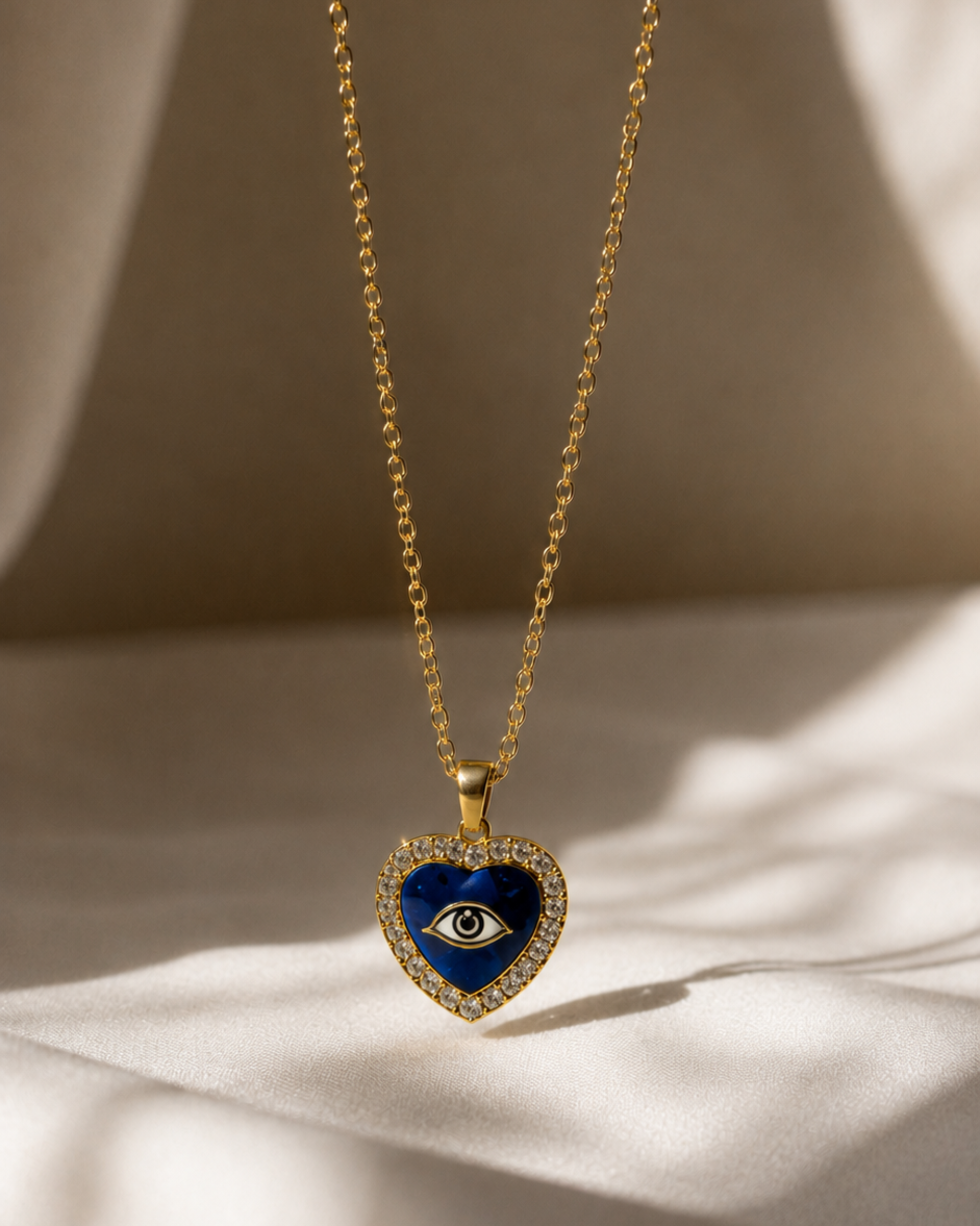 Gold necklace with a blue heart-shaped pendant featuring an eye design on a beige background