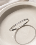 A thin silver band ring with a row of small clear stones, photographed resting on a white ceramic dish.
