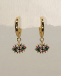 A pair of gold huggie hoop earrings with dangling evil eye charms embellished with green, blue, pink, and white rhinestones, displayed against a light gray background.