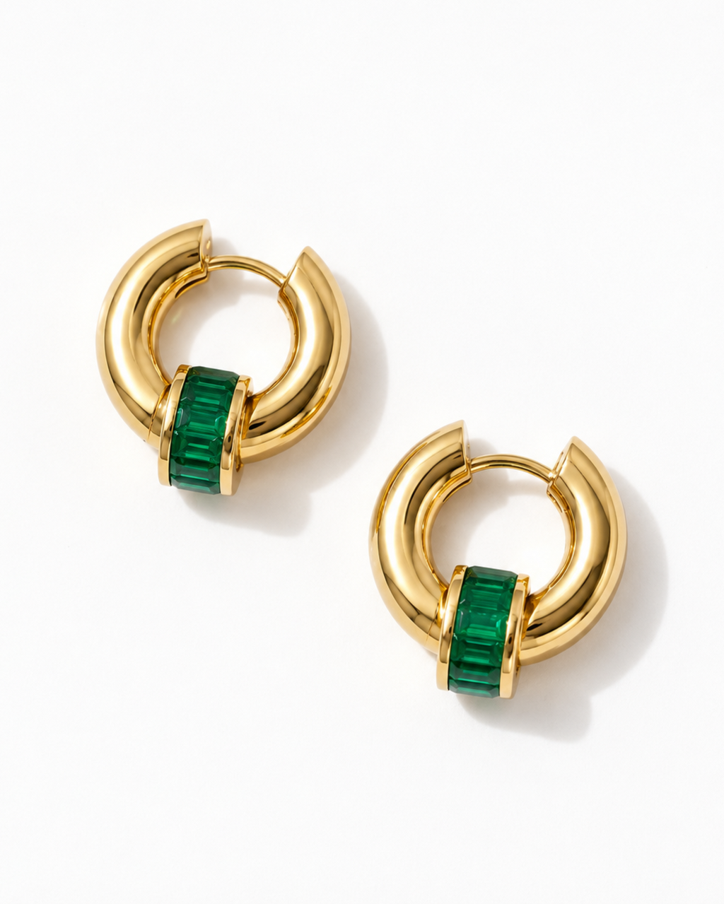 A pair of gold huggie hoop earrings with a central green emerald-cut stone, displayed on a clean white background.