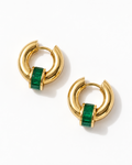 A pair of gold huggie hoop earrings with a central green emerald-cut stone, displayed on a clean white background.