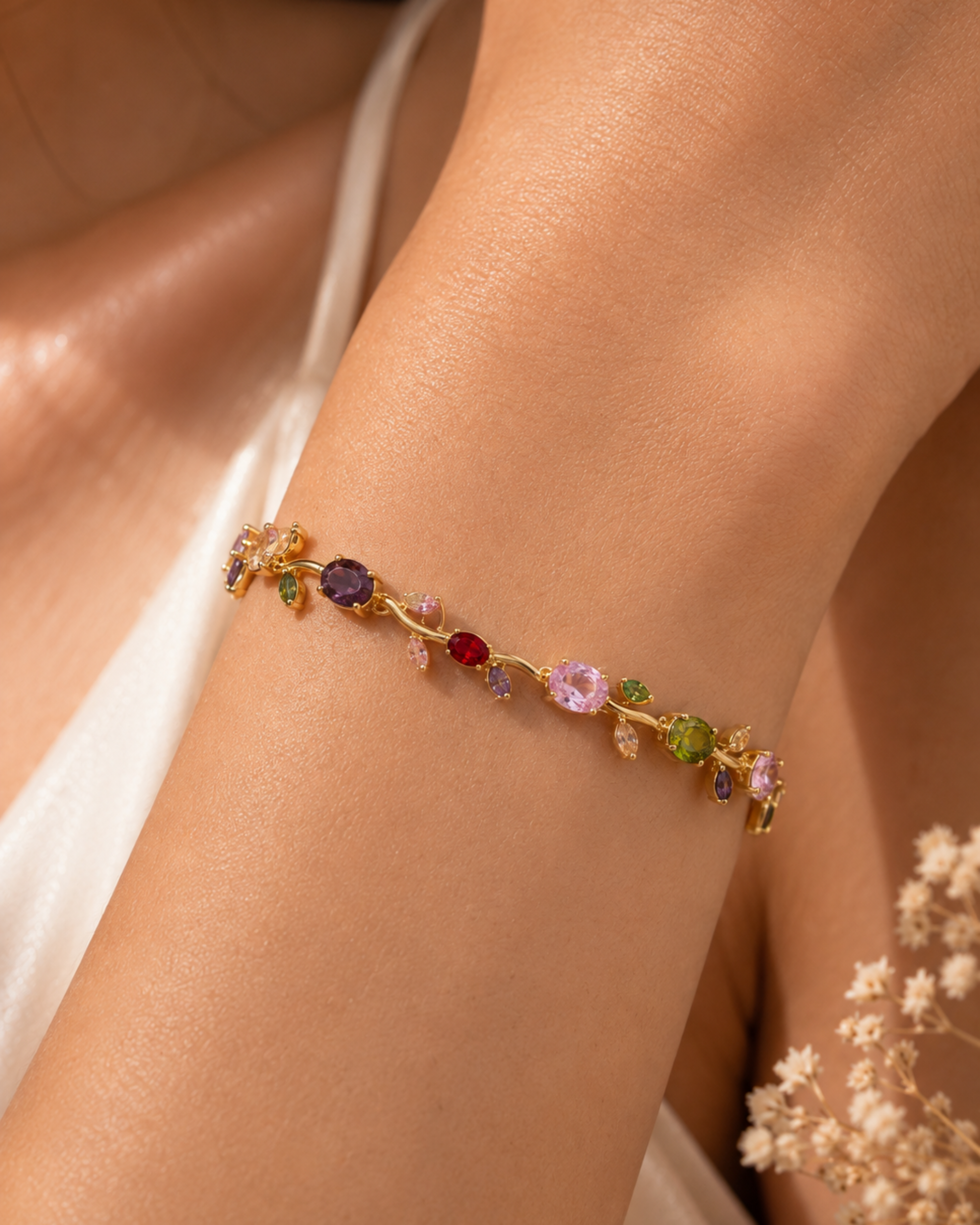 A delicate gold bracelet with colorful gemstones, worn on a woman's wrist. The bracelet features a gold-toned vine design adorned with various round and oval gemstones in purple, red, pink, green, and blue.