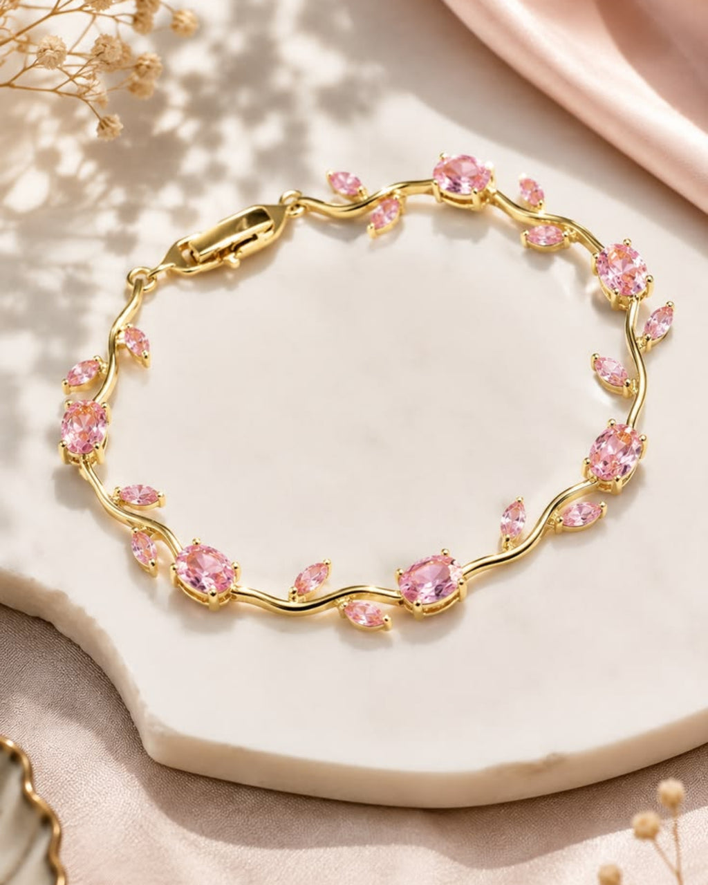 Gold bracelet with pink gemstones on a light surface with dried flowers.