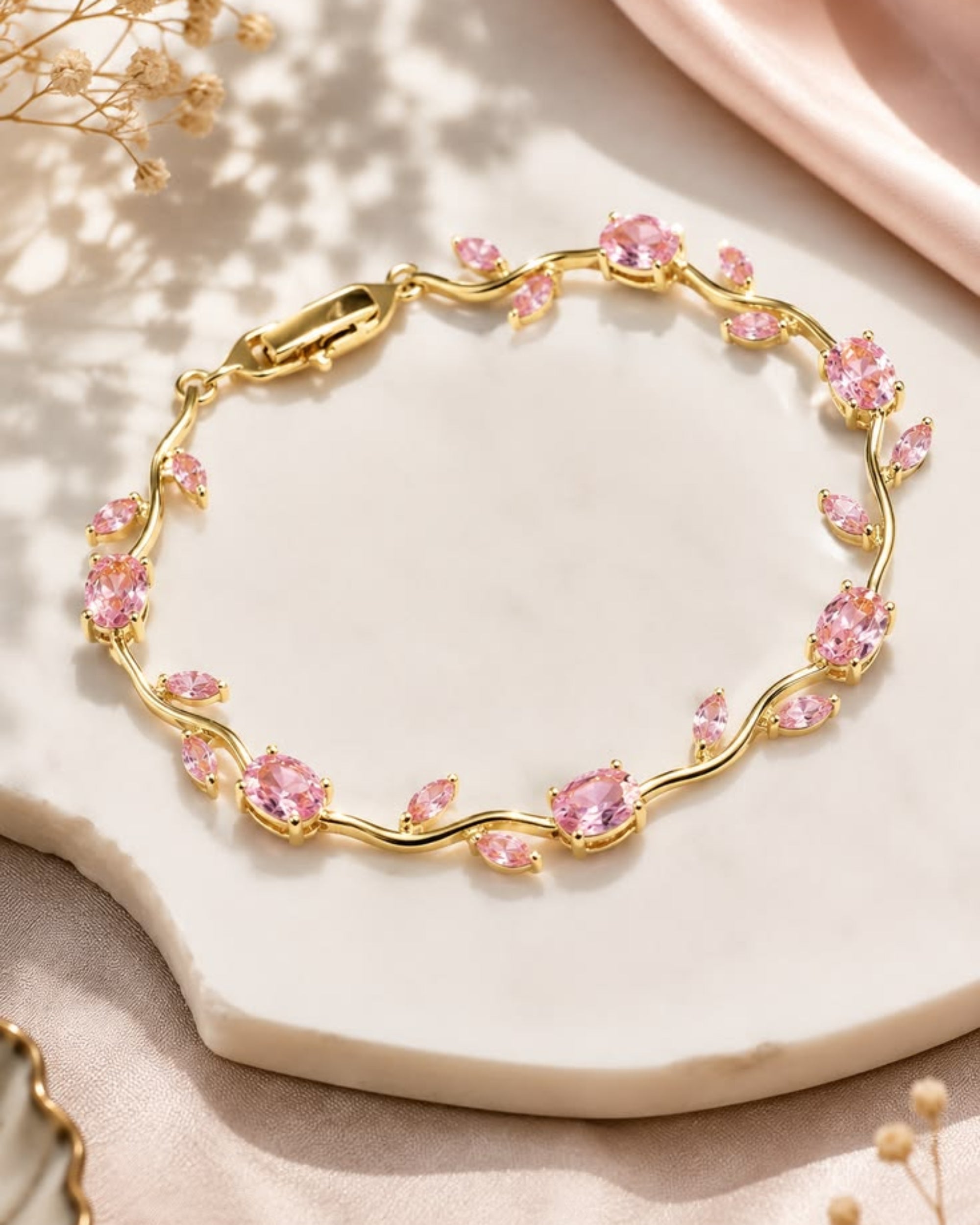 Gold bracelet with pink gemstones on a light surface with dried flowers.