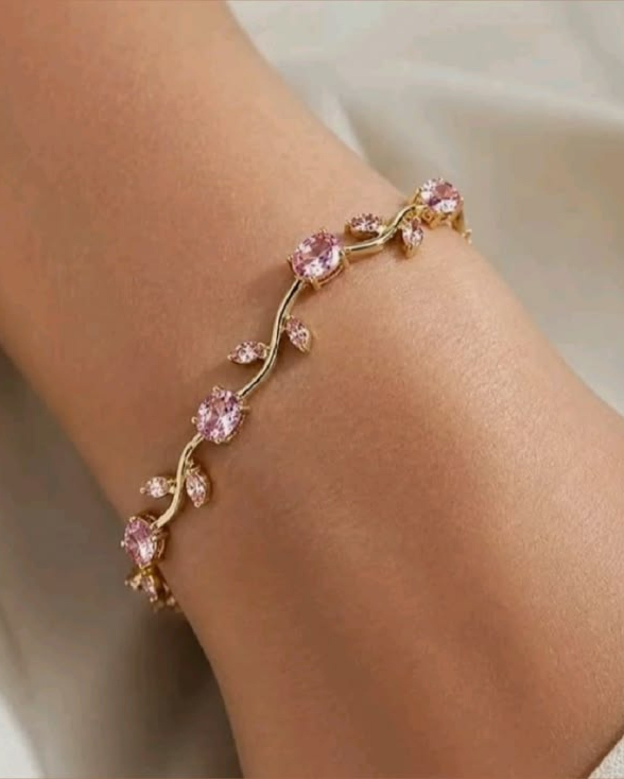 Gold bracelet with pink gemstones on a wrist against a neutral background