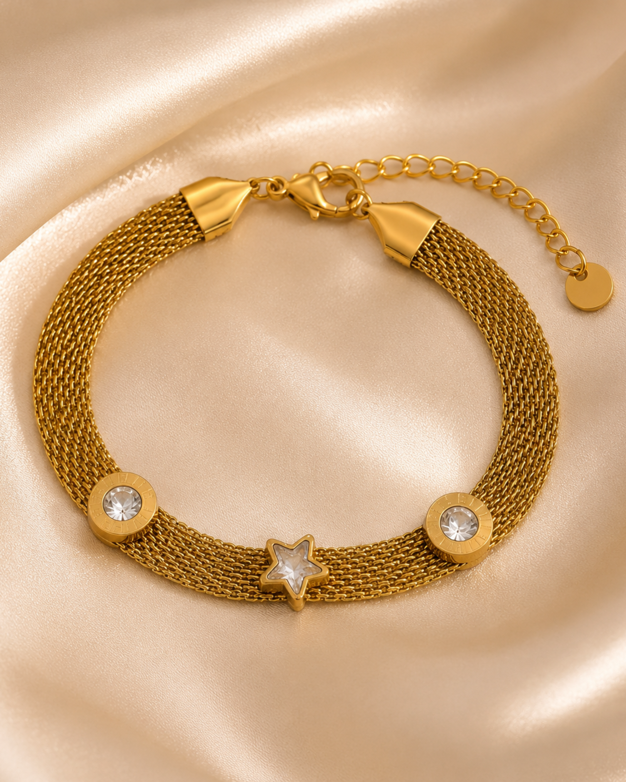 A gold-toned mesh bracelet with a star-shaped centerpiece and two round clear crystal accents, displayed on a satin fabric background.