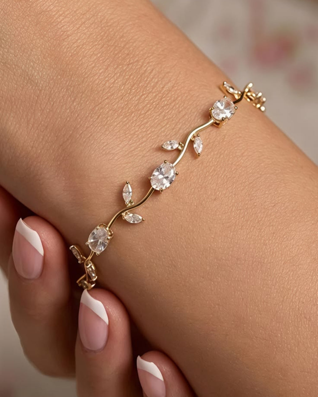 A delicate gold vine bracelet with clear crystal-like round and marquise-cut stones, shown worn on a woman's wrist with manicured nails visible.