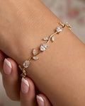 A delicate gold vine bracelet with clear crystal-like round and marquise-cut stones, shown worn on a woman's wrist with manicured nails visible.